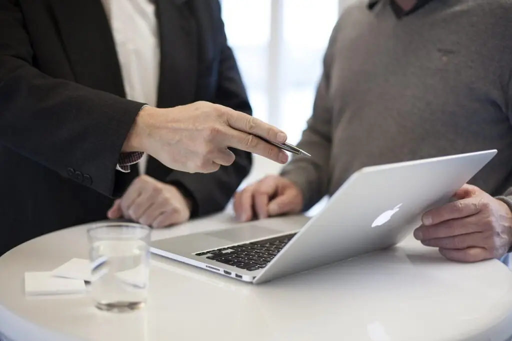 two people in a business meeting pointing at a laptop screen while discussing information